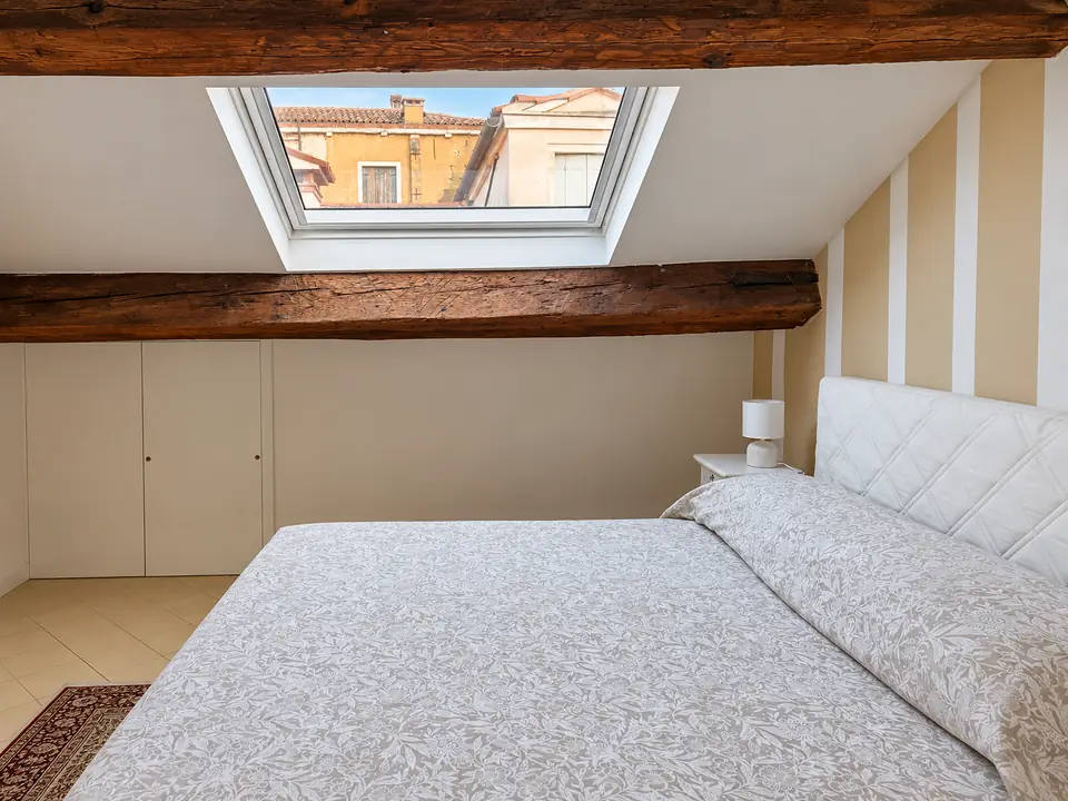 Dal letto, il lucernario tra due travi antiche e i tetti di Venezia