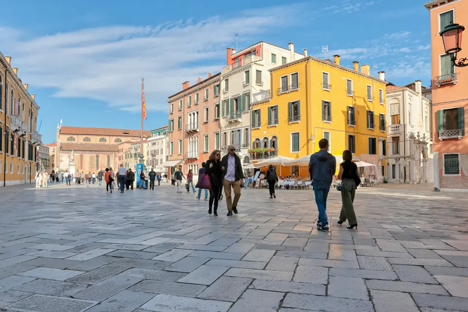 Un campo veneziano con case gialle e persone a passeggio